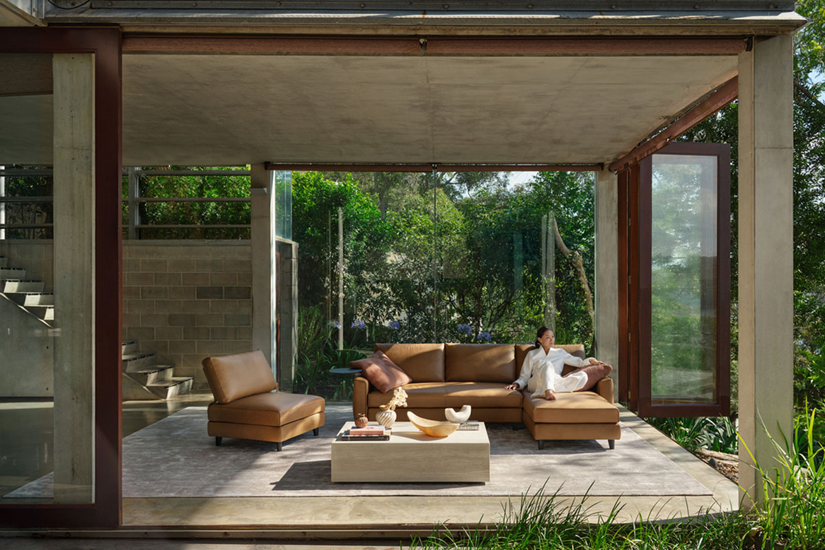 Living spaces with raw concrete and greenery, deep earthy seating, and natural textures layered through rugs and surfaces.