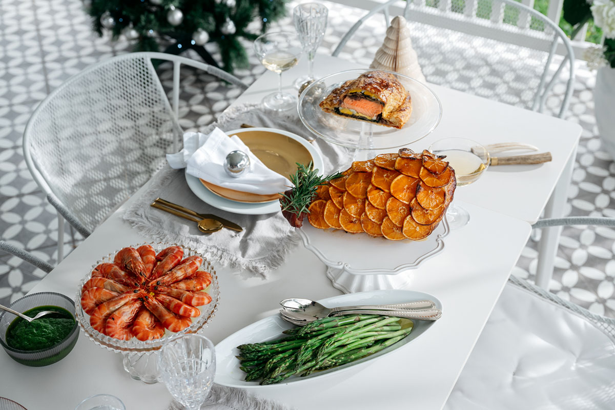 An outdoor dining setting styled for a Christmas lunch with sculptural dining chairs, a white ceramic dining table, and festive food.