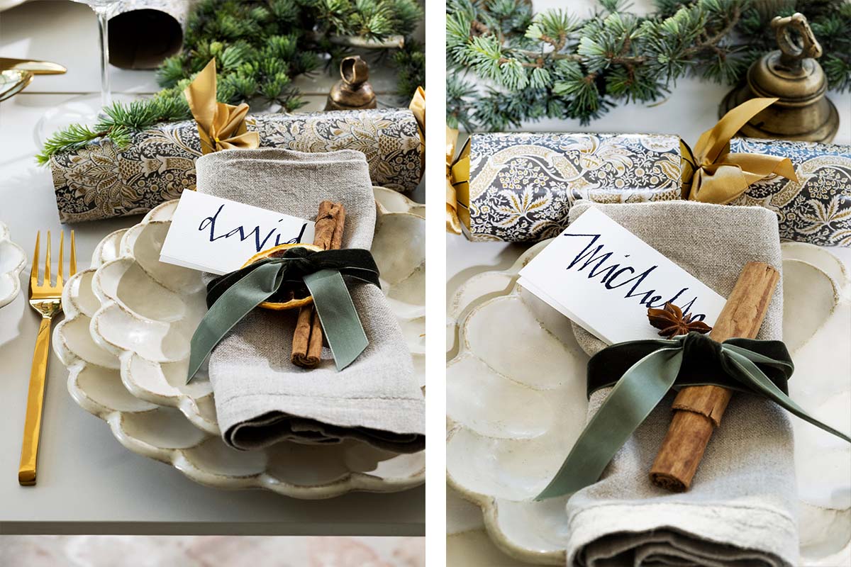 Two place settings featuring scalloped cream and gold plates, handwritten place cards, deep green accents, and gold cutlery on textured linen.