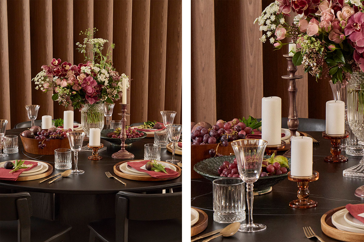 A black timber dining setting styled abundantly with gold cutlery, maroon linens, reflective décor, fruits and florals.