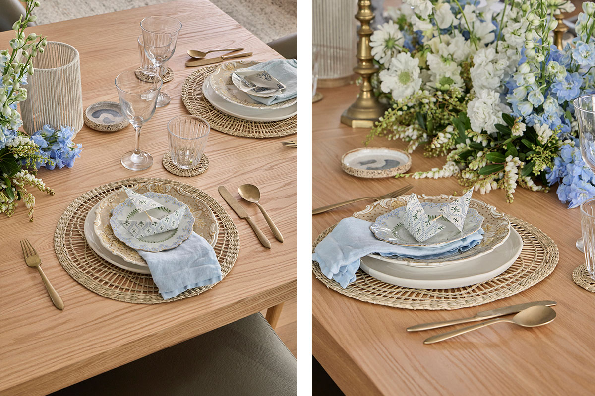 A light timber dining setting styled with pastel blue and white florals, origami boats, rustic gold cutlery and rattan placemats.