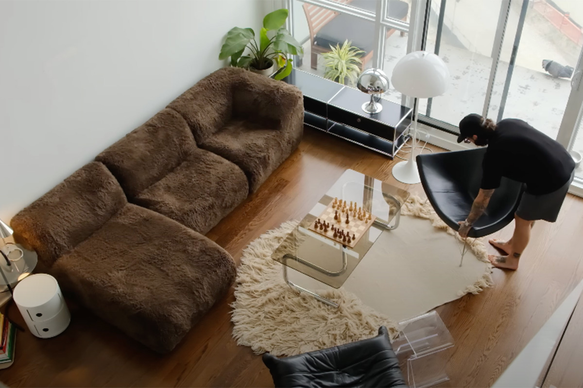 Digital Creator Charles Mackenzie sits in his compact loft-style apartment, styled with a King Living 1977 Modular Sofa in Yowie Chocolate, a deep brown faux fur fabric.