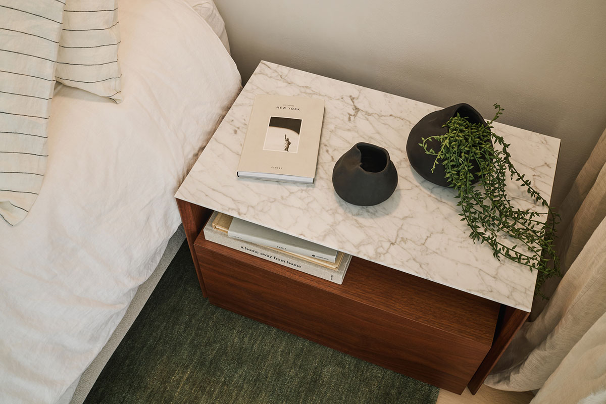 Timber bedside table with a marble top styled with greenery, design books, and a ceramic teapot.