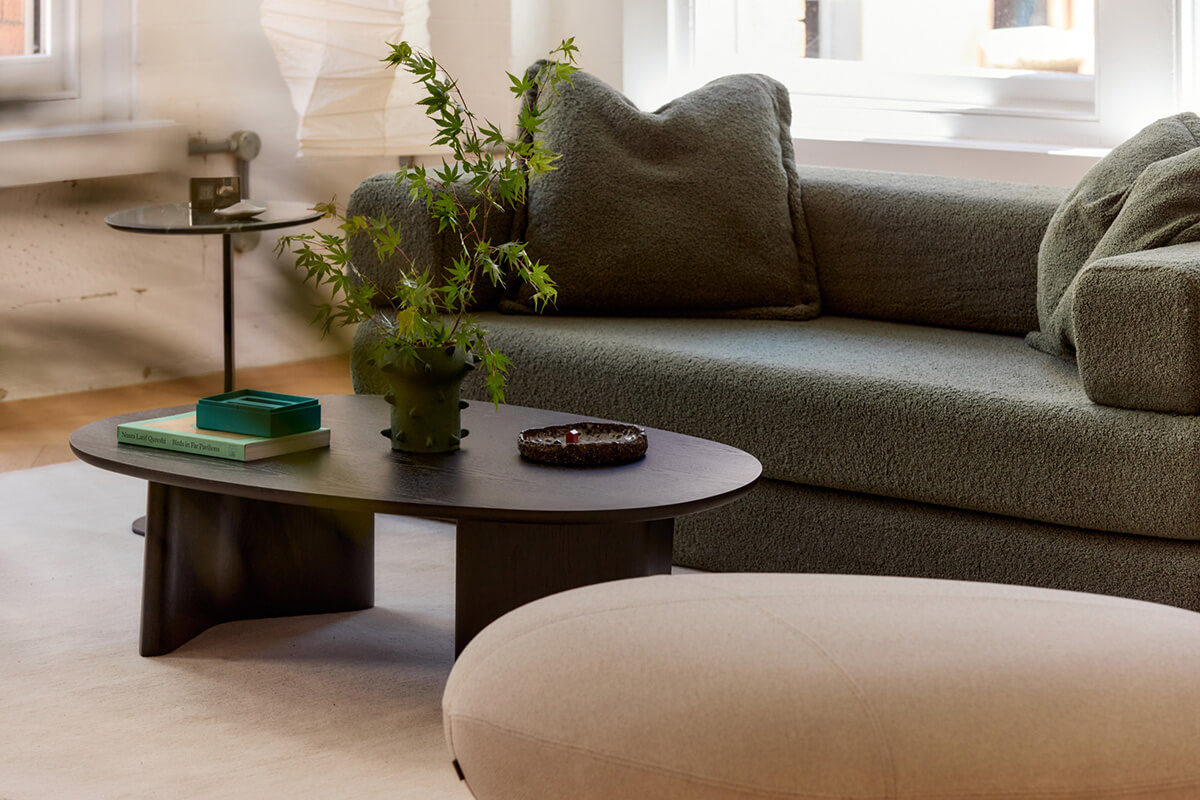 Two hygge-inspired lounge settings with curved sofas, styled in natural light with green accents on low coffee tables.