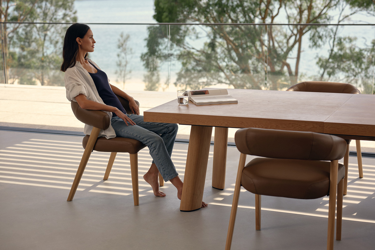 Woman sits at a modern dining table and gazes out a window.