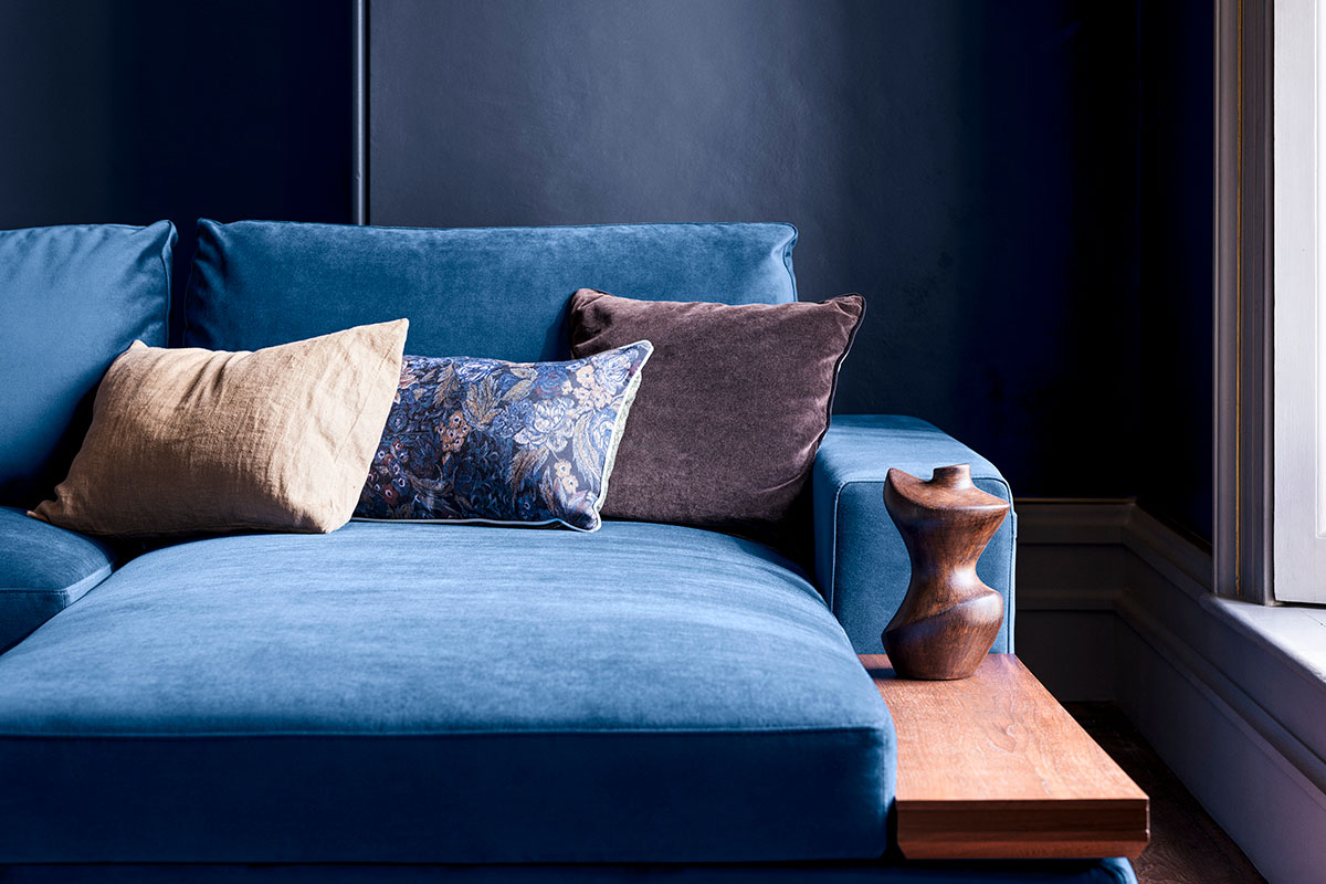 Close up of a blue sofa with three scatter cushions against a blue wall.