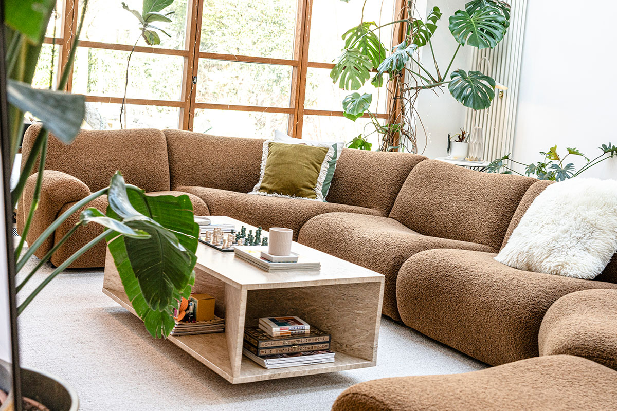 Modern living room with a curved caramel bouclé sofa and lush indoor greenery surrounding a marble coffee table