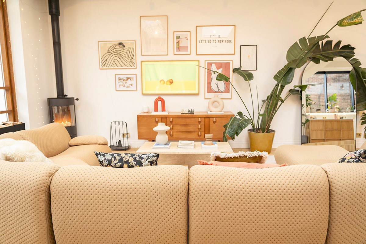 Modern living room featuring a curved tan sofa, a gallery wall, and a wooden sideboard with curated decorative accents and greenery.