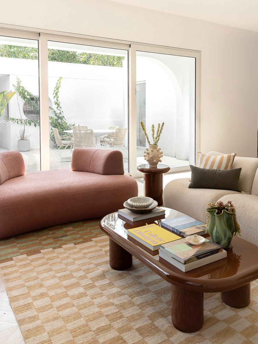 Curved forms of the Aura Sofa and 1977 Sofa bring warmth and flow to a contemporary living space, grounded by the structured geometry of the rug and architectural glazing.