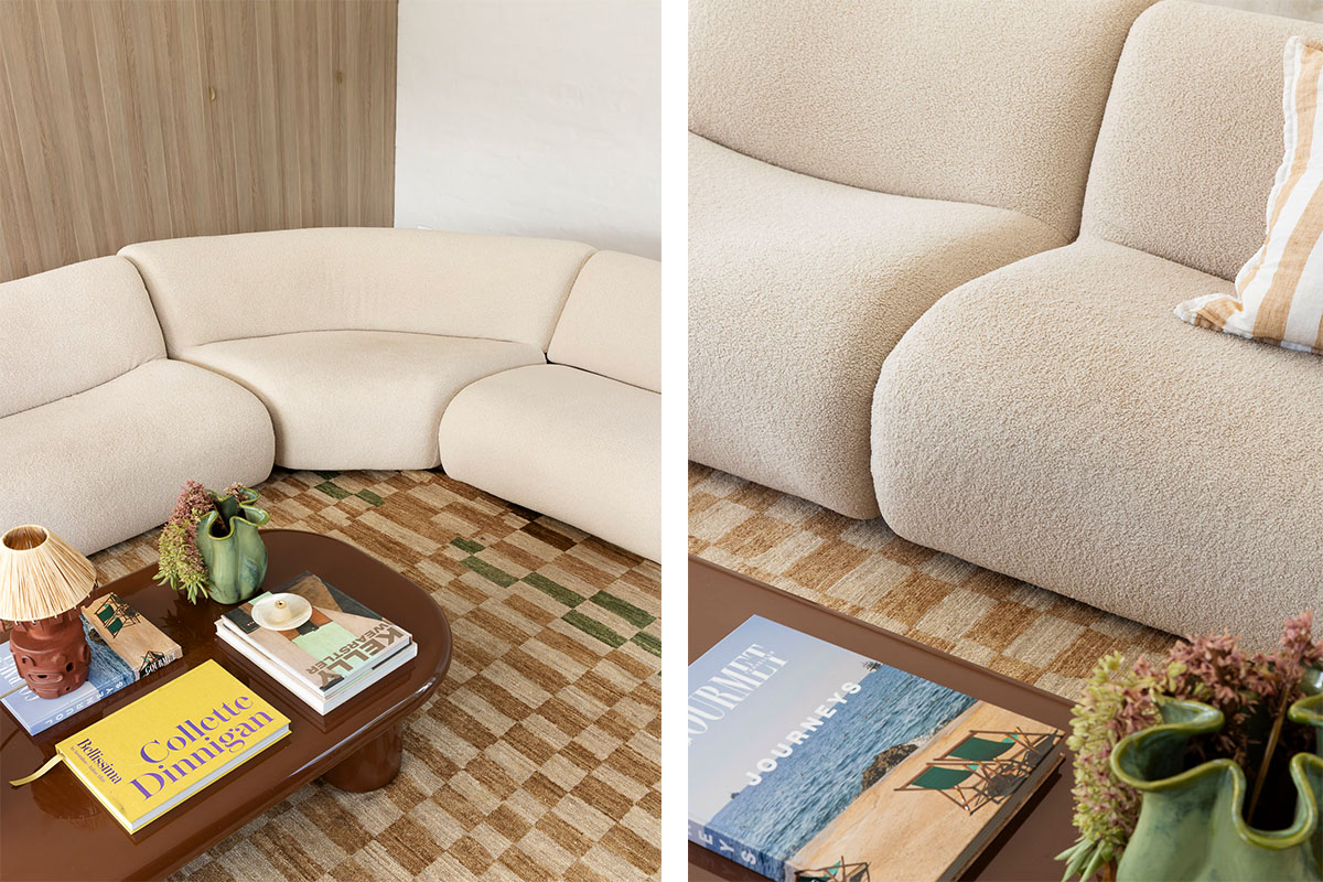 A contemporary living space framed by a softly curved modular sofa in textured beige fabric, styled with a mid-century inspired coffee table and check-patterned rug in earthy tones.