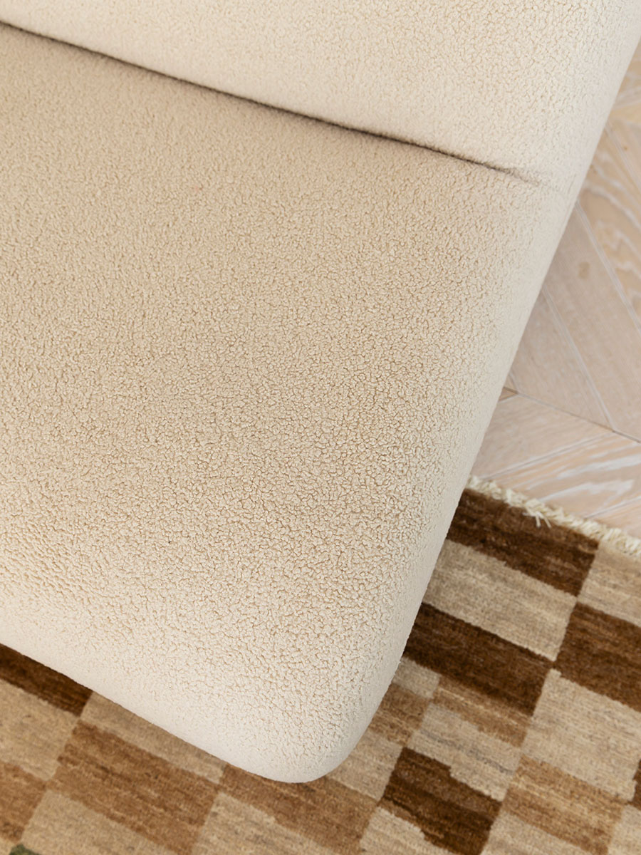 Close-up of a curved sofa in textured bouclé fabric, with soft, natural tones complementing the earthy geometry of the rug below.
