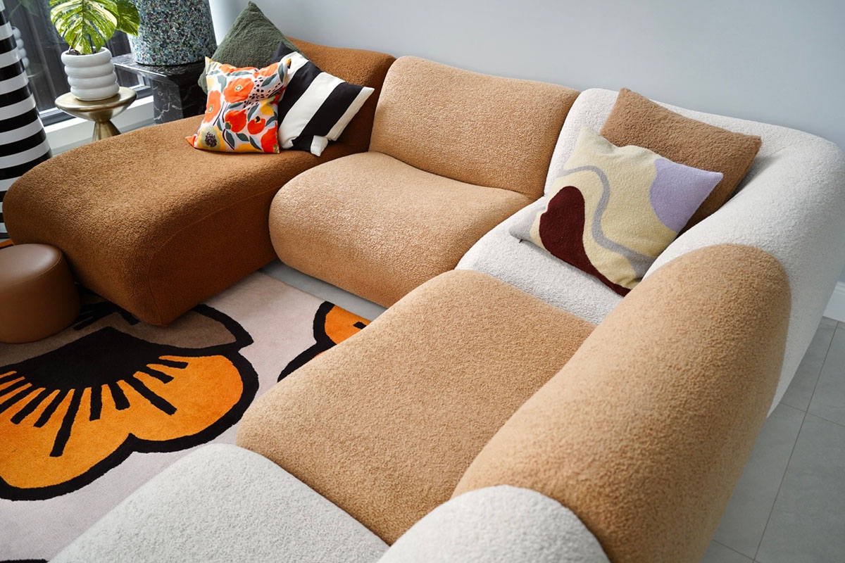 Close-up of a curved modular sofa in neutral tones styled by Katherine Sabbath, featuring rich textural contrast, sculptural curves and layered cushions on a floral statement rug.