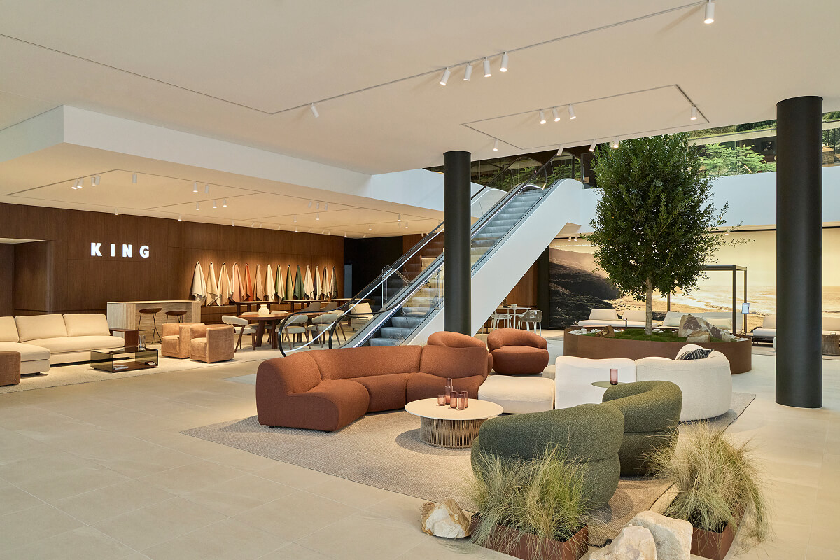 Nature-inspired living space with earthy green hues, soft-toned seating and sculptural coffee table framed by bushland views.