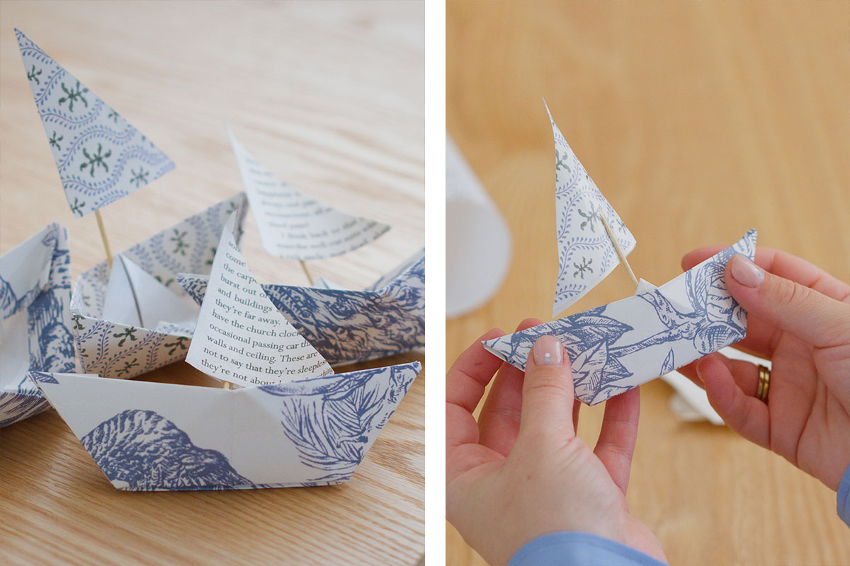 Three images of a blue and white origami boat positioned on top of each plate at a coastal-styled table setting.