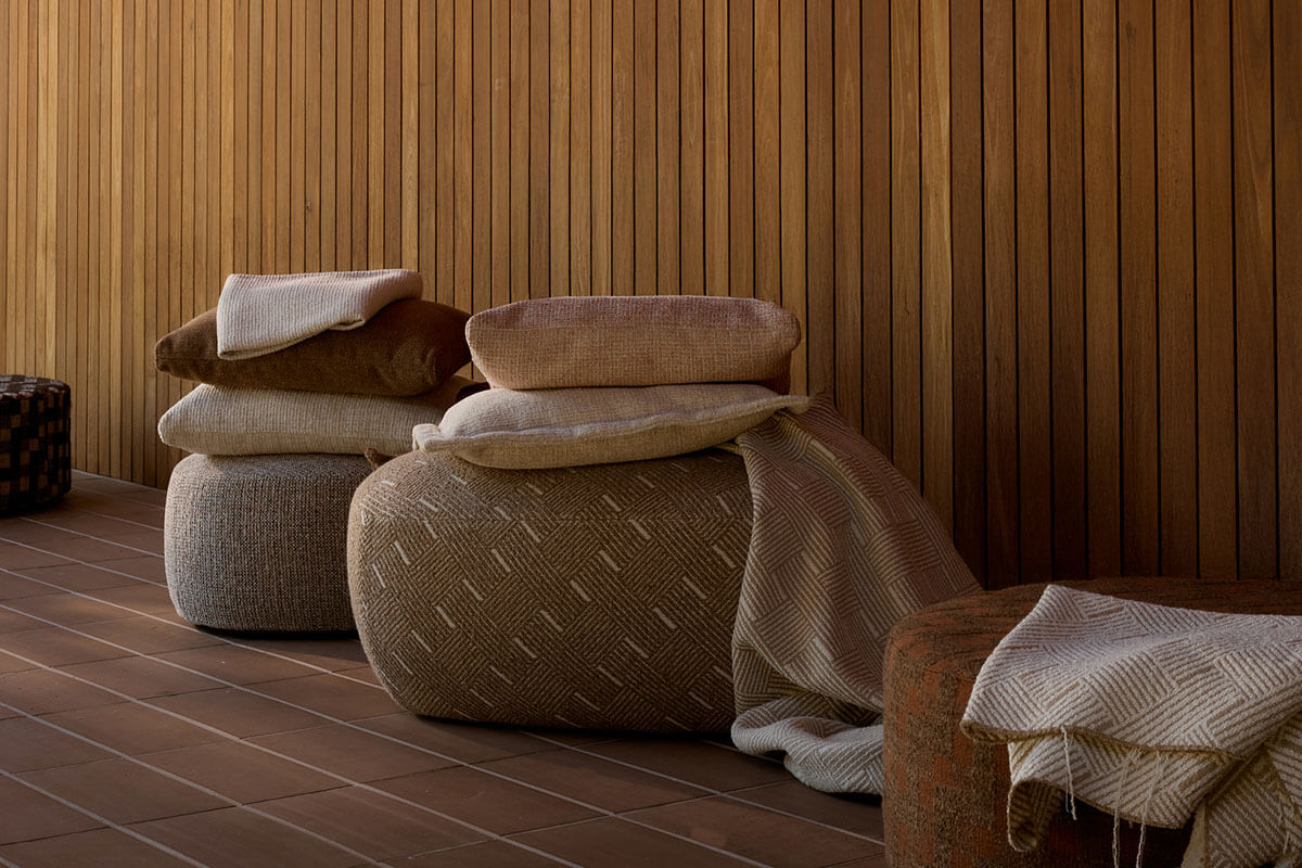 Round woven ottomans with stacked cushions and a draped throw styled on terracotta tiles and timber paneling.