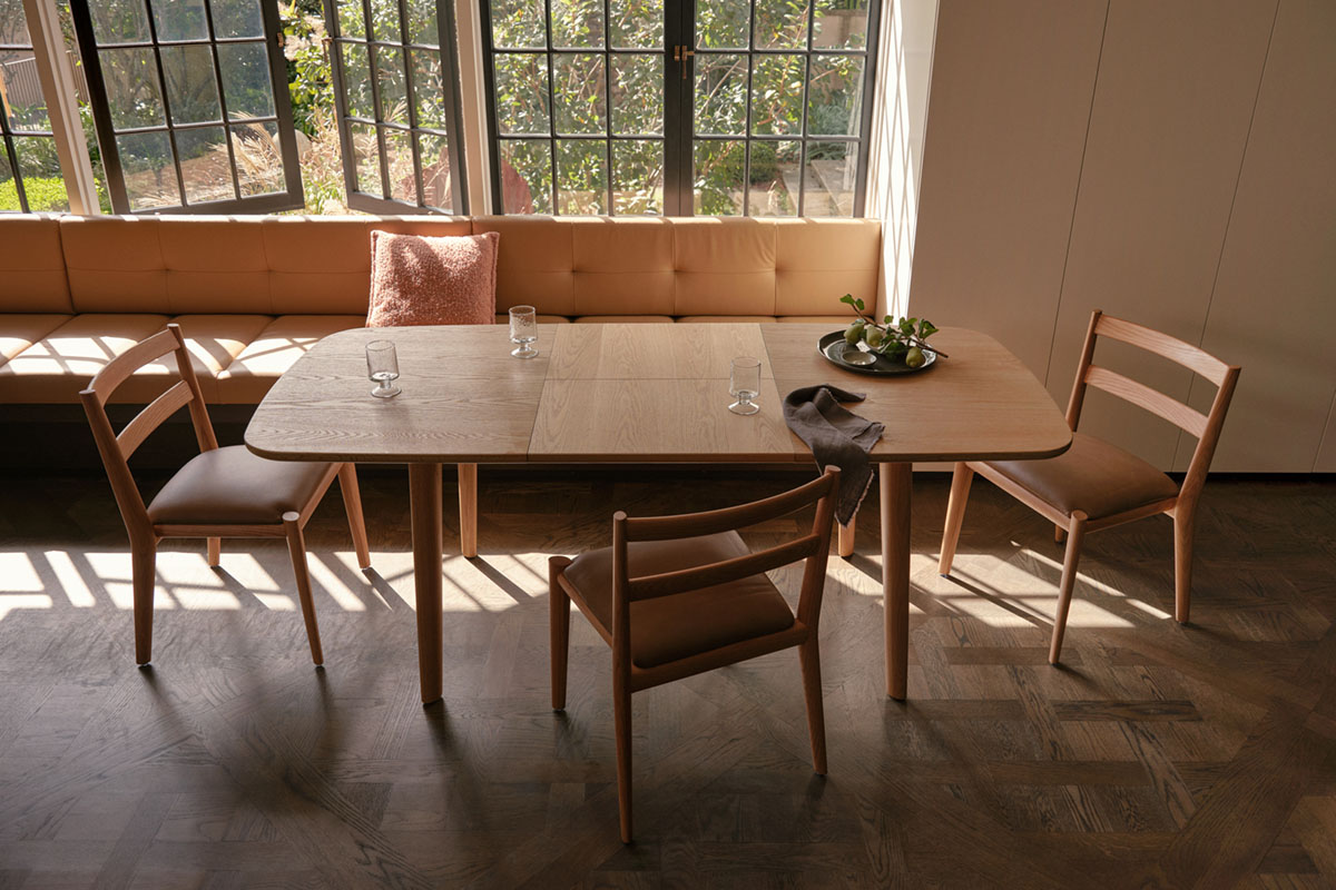 Modern extendable dining table and chairs in a light oak timber, positioned near window with natural light filtering through.