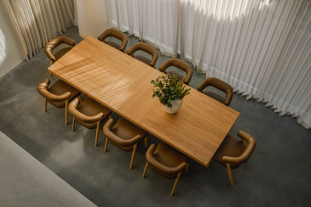 A rectangular dining table shot from above in a light brown timber, styled with curved leather dining chairs against a concrete floor.