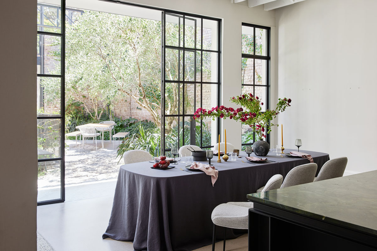 Oval dining table dressed with a navy linen tablecloth in a contemporary dining space with lots of natural light.