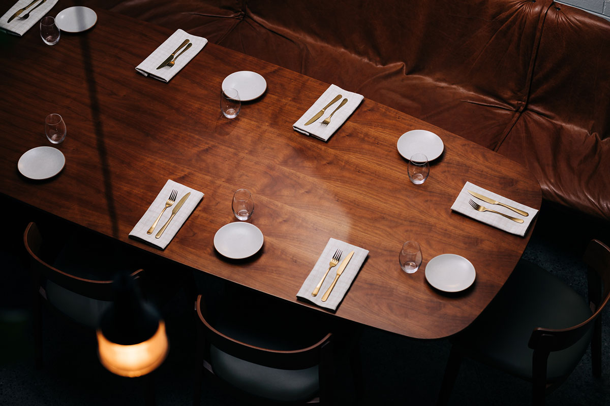 A contemporary oval dining table in warm timber styled minimally with hanging pendant lights above for ambience.