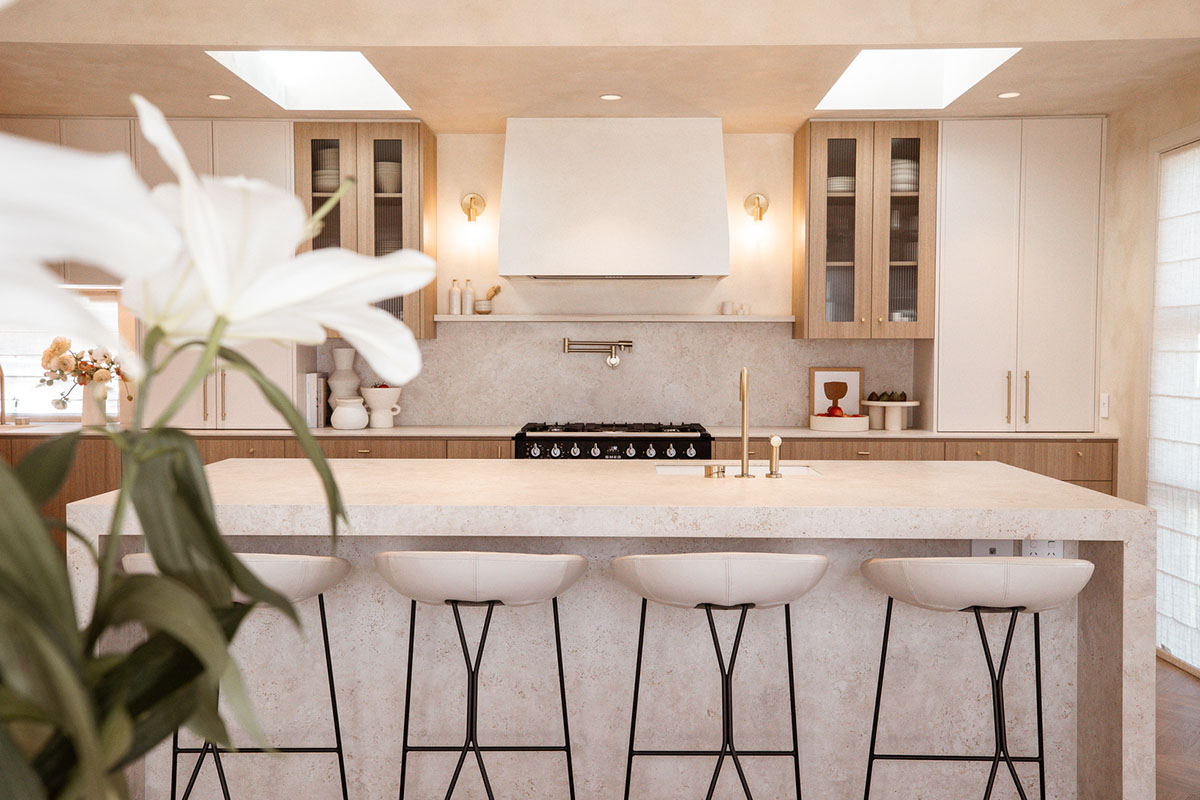 Modern kitchen island with industrial counter stools featuring soft white leather seats and black steel frame legs.