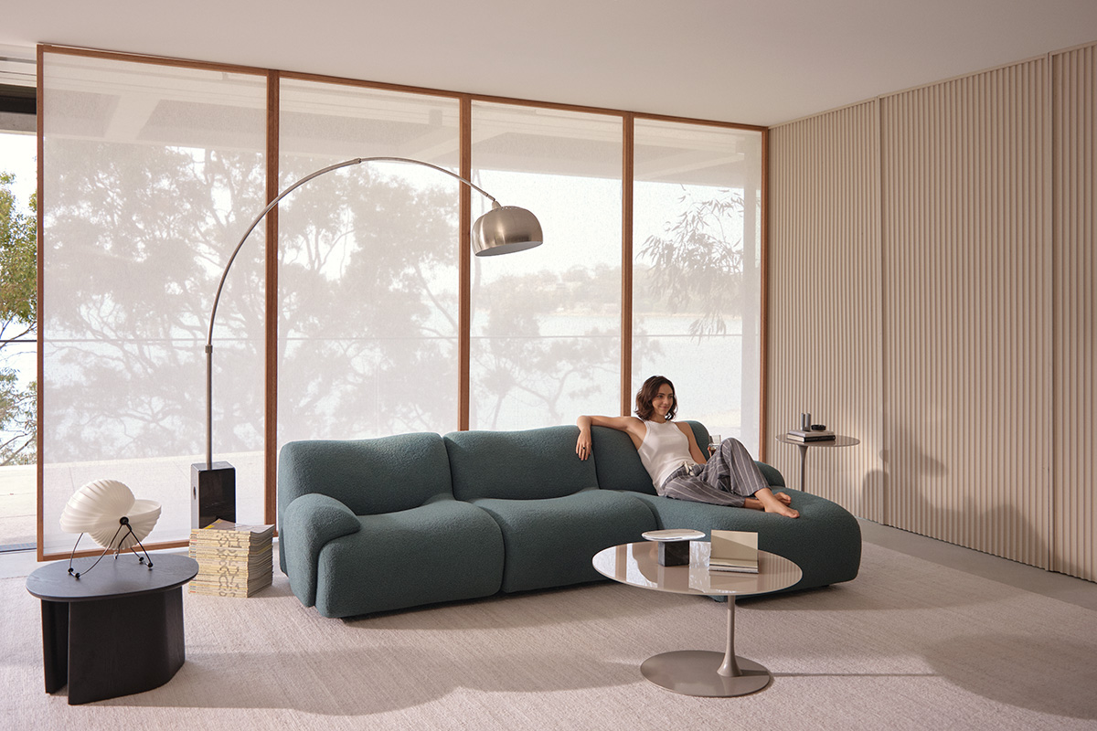 A woman relaxes on a modern teal modular sofa in a bright, minimalist living room.