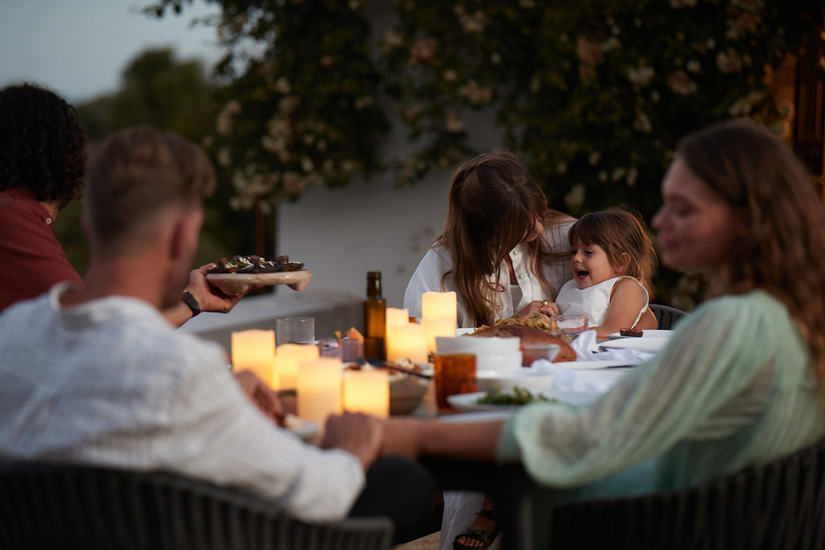 Family and friends enjoy an outdoor evening meal around a contemporary dining table, styled with ambient candles and festive food.