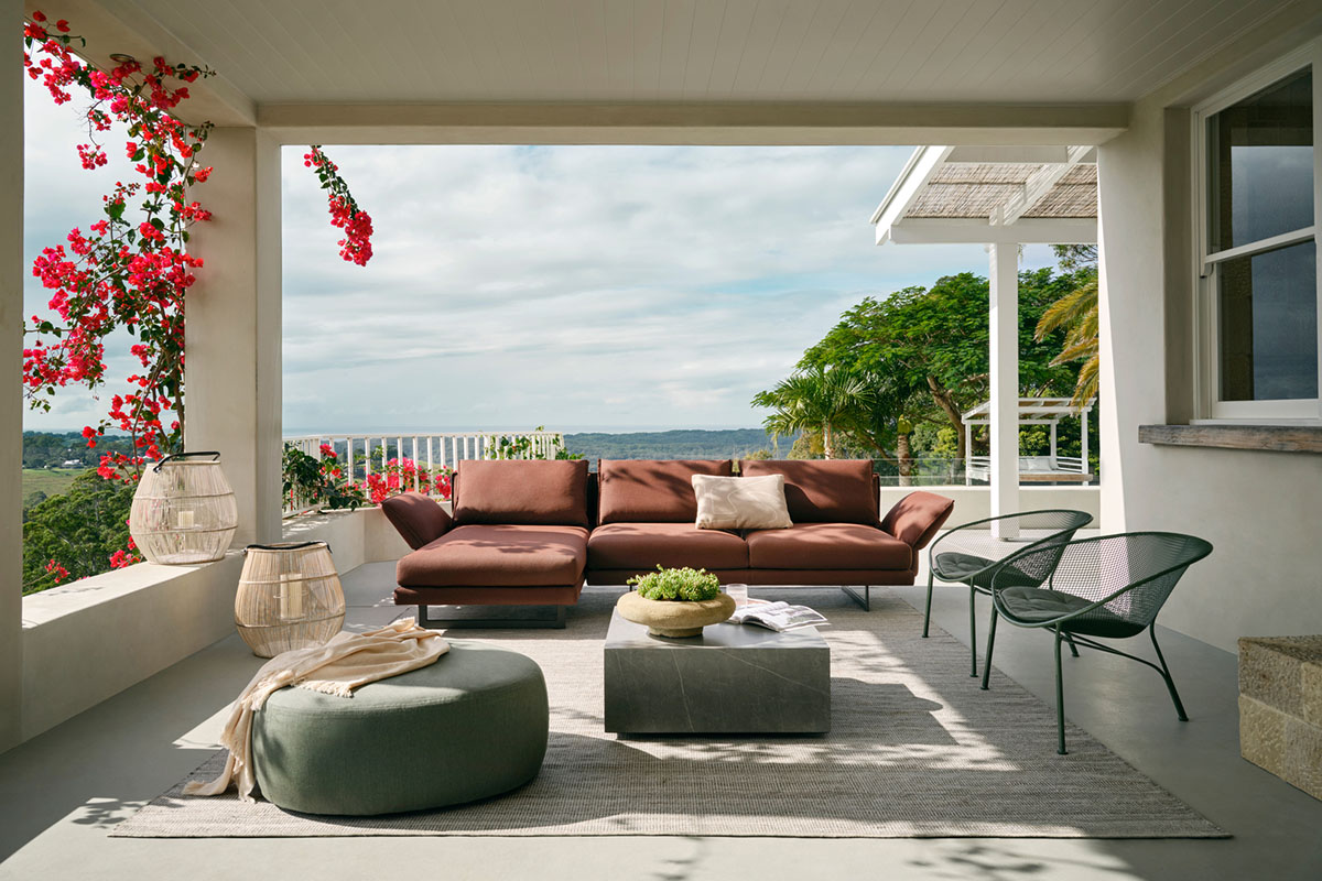 A shaded patio setting with a warm terracotta brown outdoor sofa styled with a modern stone coffee table, ottoman and outdoor occasional chairs.