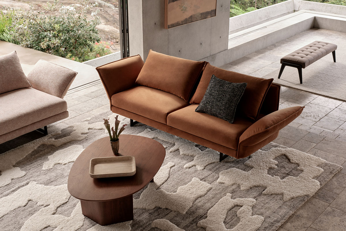 A living room with warm tan sofa, textured neutral rug and soft earthy timbers and tones framing an autumn-inspired palette.