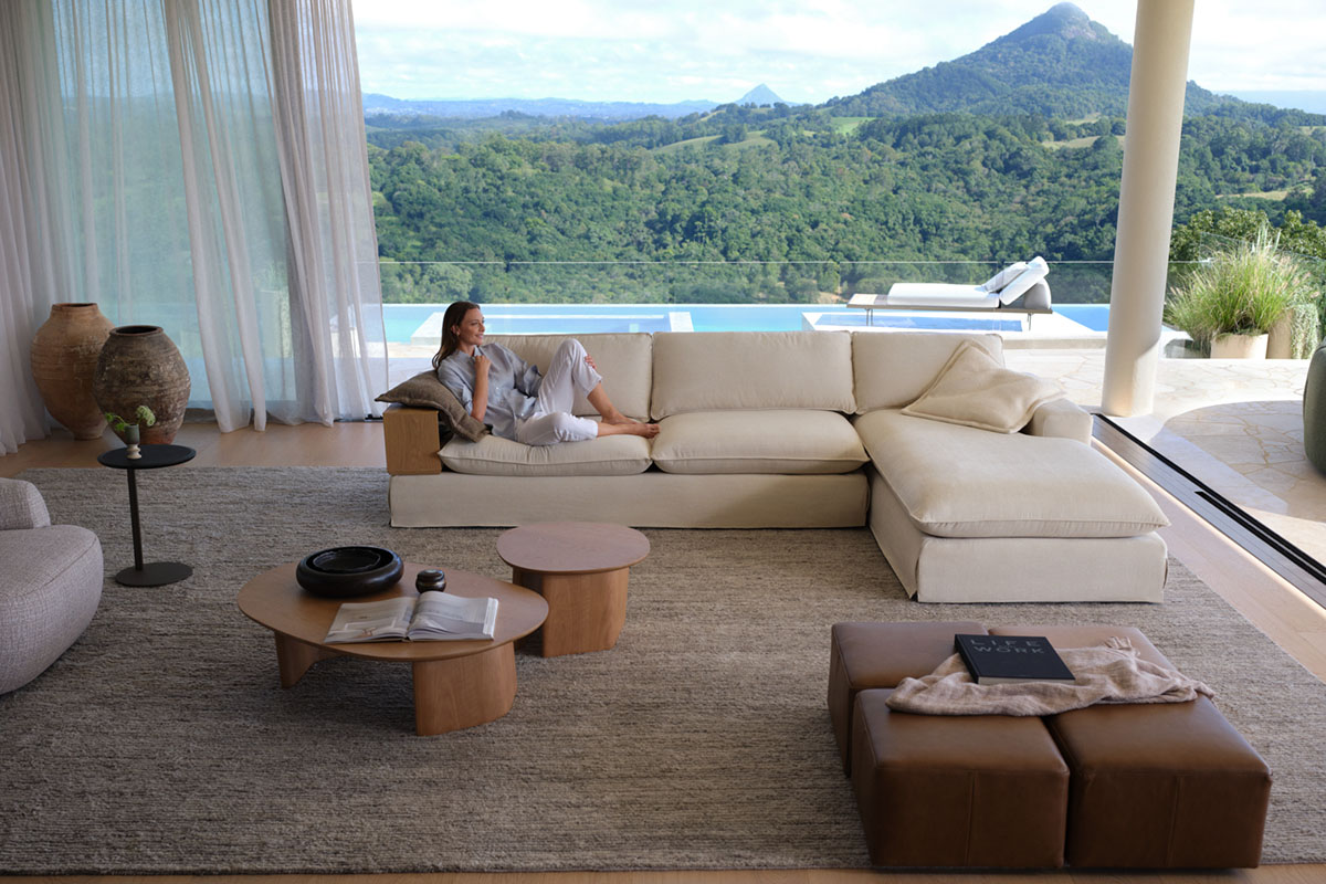 An airy, bright contemporary living space styled with a neutral modular sofa with floor-to-ceiling windows opening out to lush mountainous views.