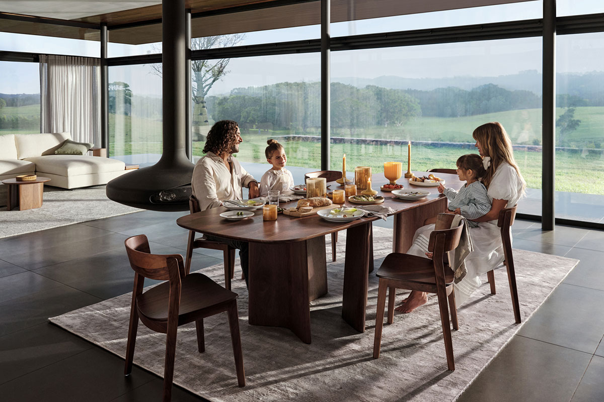 A family enjoy a winter lunch around a festive dining table with landscape views. The setting is warm with deep-toned timber dining furniture, decorated seasonally.