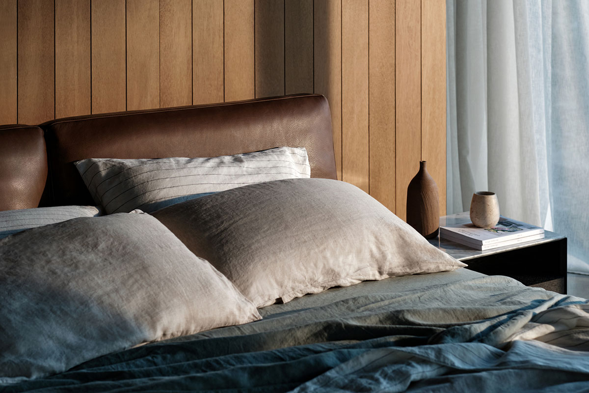 A warm bedroom setting with a chocolate brown leather bedhead and bedding styled in shades of neutrals and ocean blues.